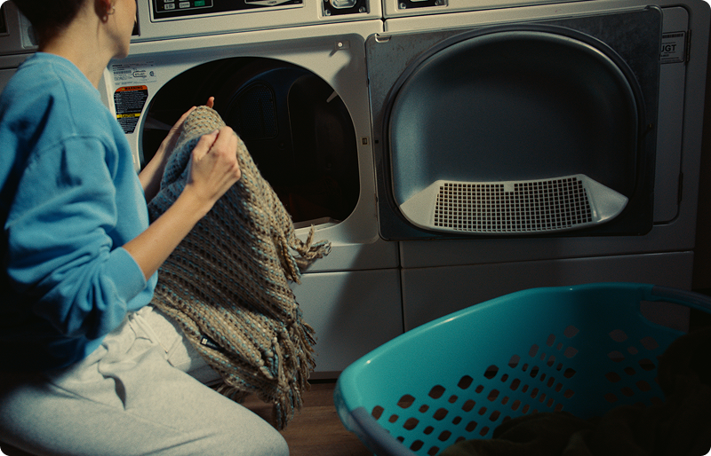 person transferring a knit blanket into a dryer